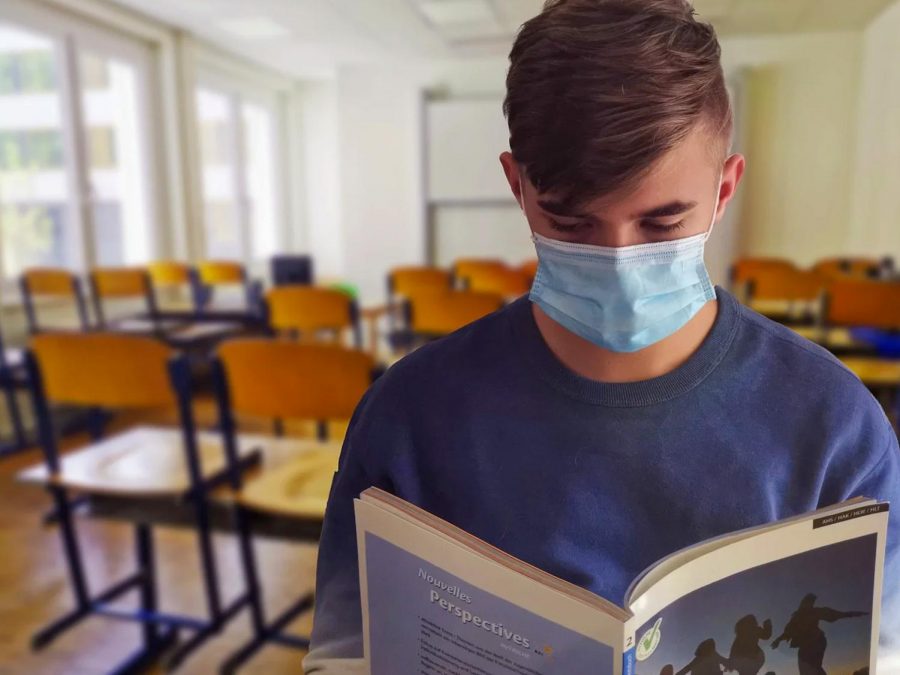 A masked student reads a book in an empty classroom. Scotch Plains-Fanwood Public Schools reopened for HS students on Jan. 19, 2021; many students now attend socially-distant, masked classes. 

