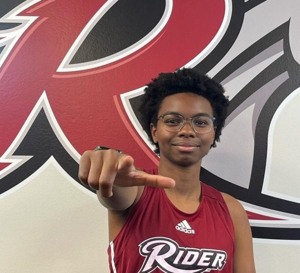 Senior Mackenzie Virgil points to the camera with the Rider University logo in the background. Virgil announced her commitment to Riders Track and Field Team on Tuesday, Feb. 13.